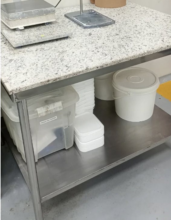 Bancada industrial em aço inox com tampo de granito, em área de produção
